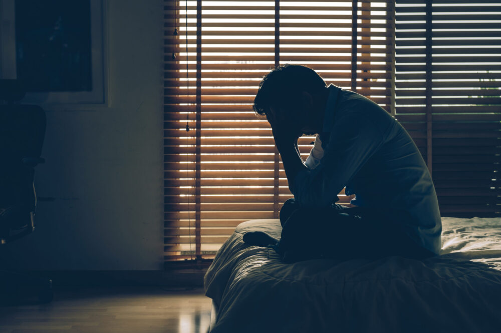 Sad businessman sitting head in hands on the bed in the dark bedroom with low light environment