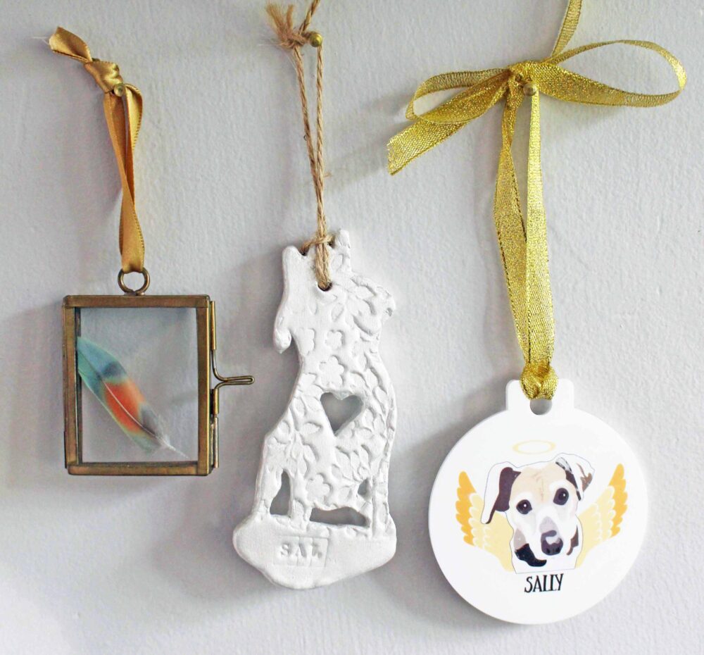 PIcture of a colourful feature in a small frame, the outline of my old dog Sal in clay, it includes a heart in the middle and her name on the base, she is wearing a crown, also a bauble with sally's face on she is black and tan and has floppy ears behind her is wings and above her head a halo it hands on gold ribbon.