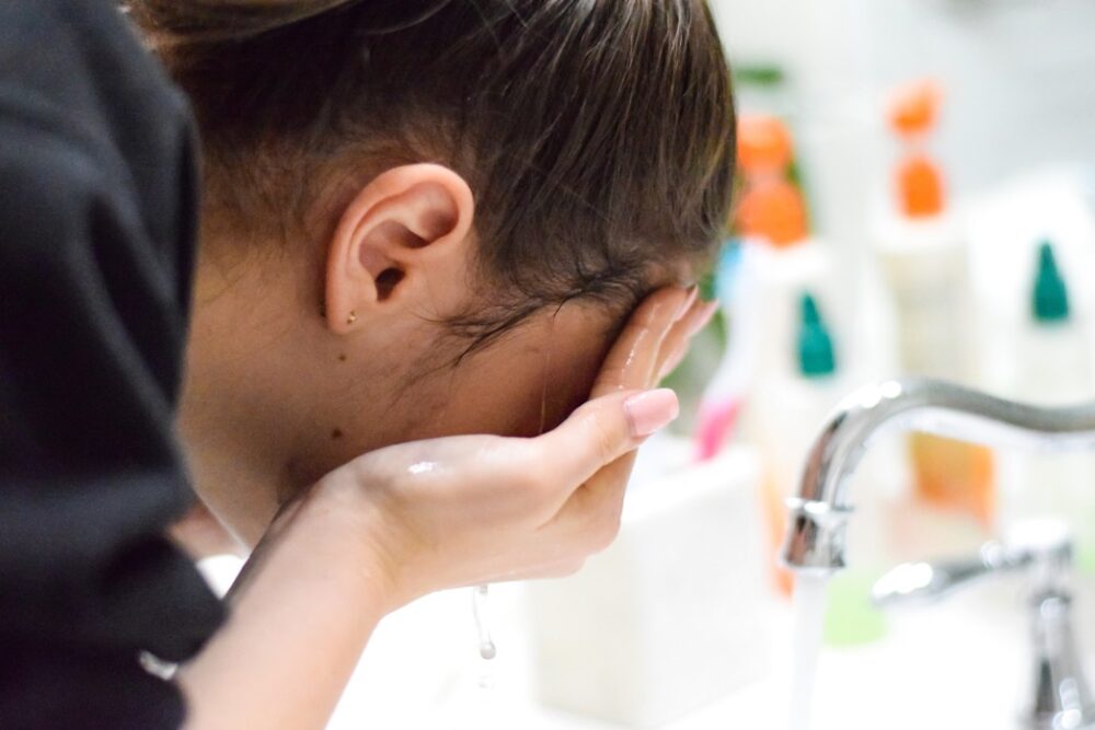 Young teenage girl washing her face over the sink