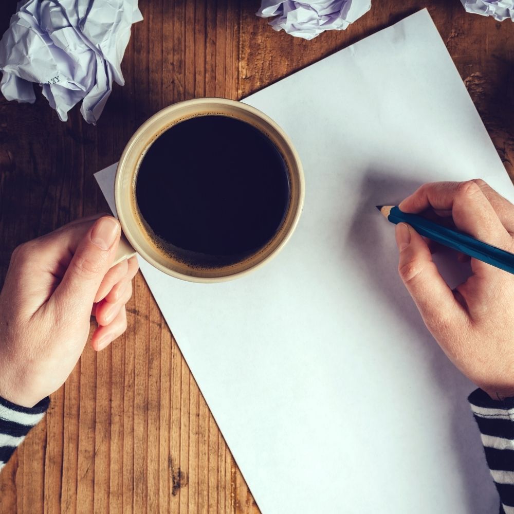 person holding a pen and a cup of coffee writing