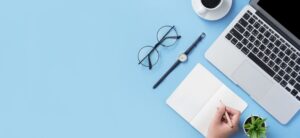someone writing in a notebook with laptop coffee glasses and watch