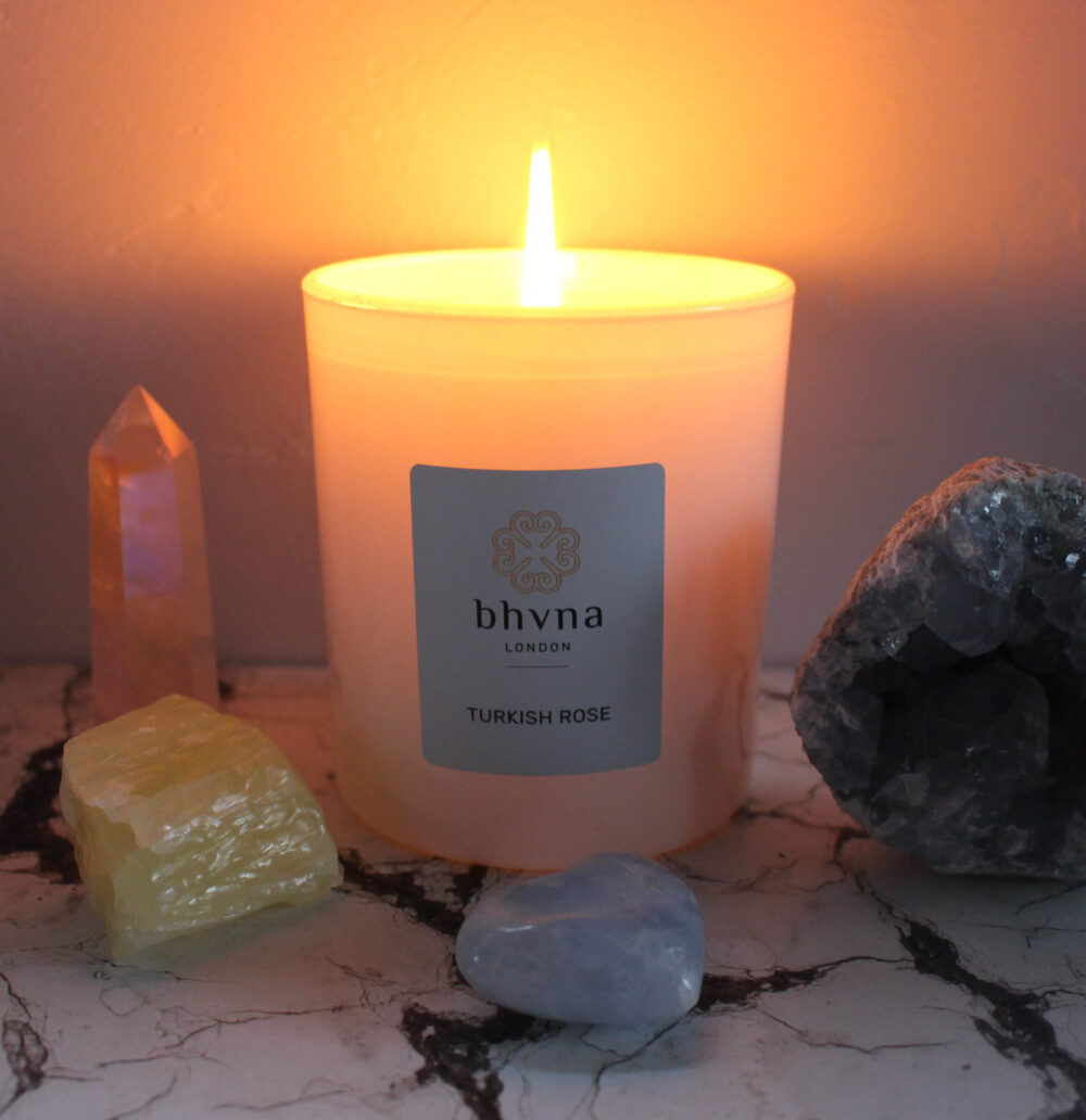 bhvna london luxury candle white glass container with the wick alight casting a yellow glow