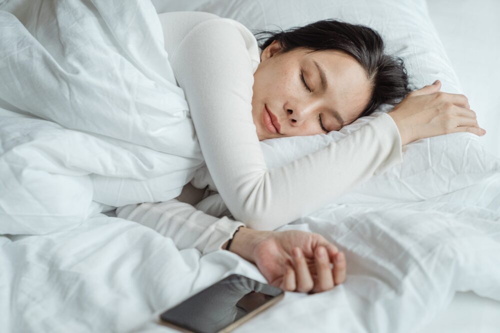 woman sleeping on a bed near a smartphone