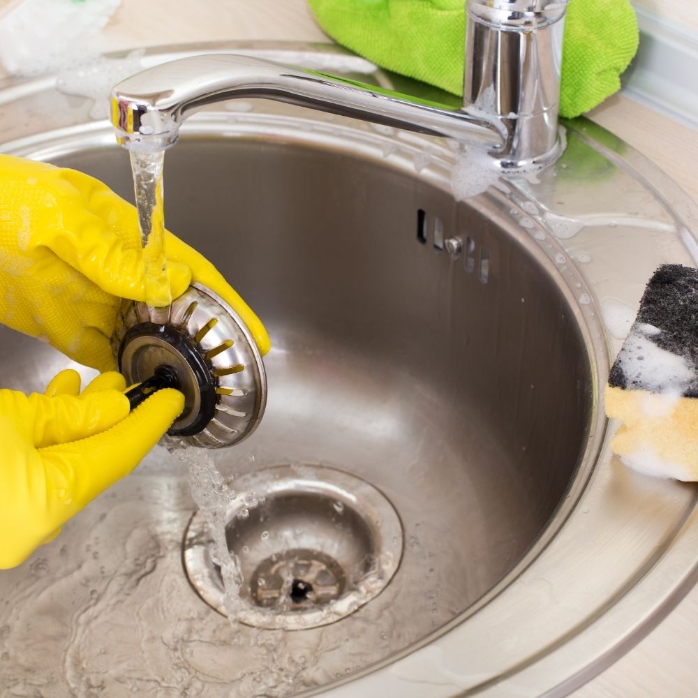 sink drain being cleaned out by person wearing yellow rubber gloves