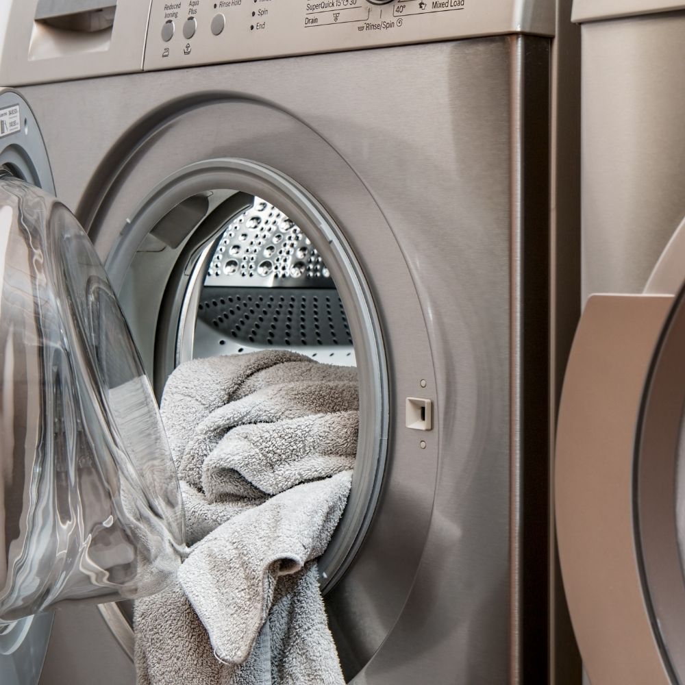 grey washing machine with the door open and laundry hanging out