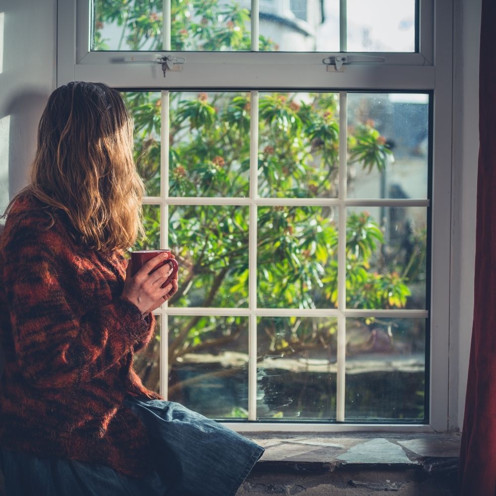 person sat looking out a window and a beautiful view hold a mug via Canva