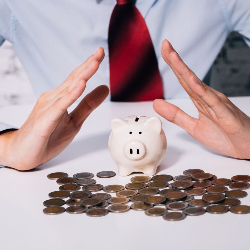 man with his hands above a piggy bank protecting it