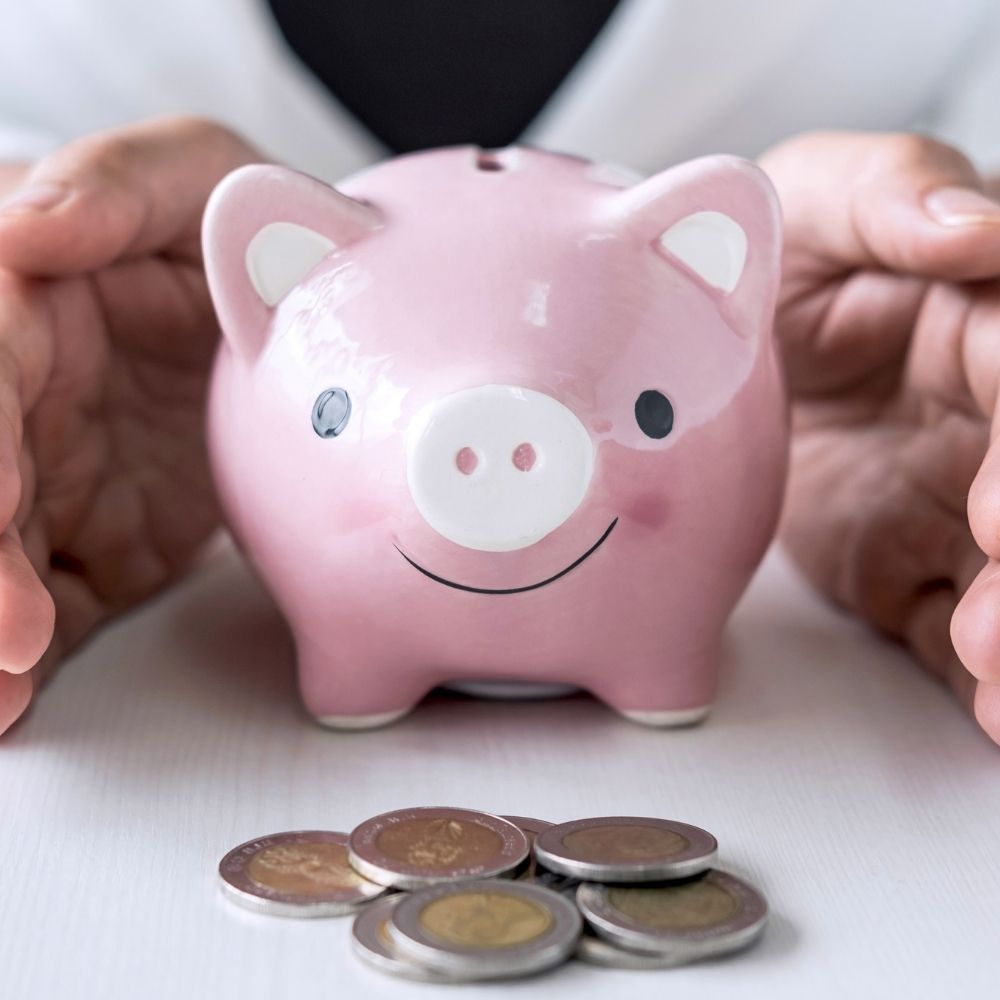 man with his hands protecting a piggy bank and coins in front
