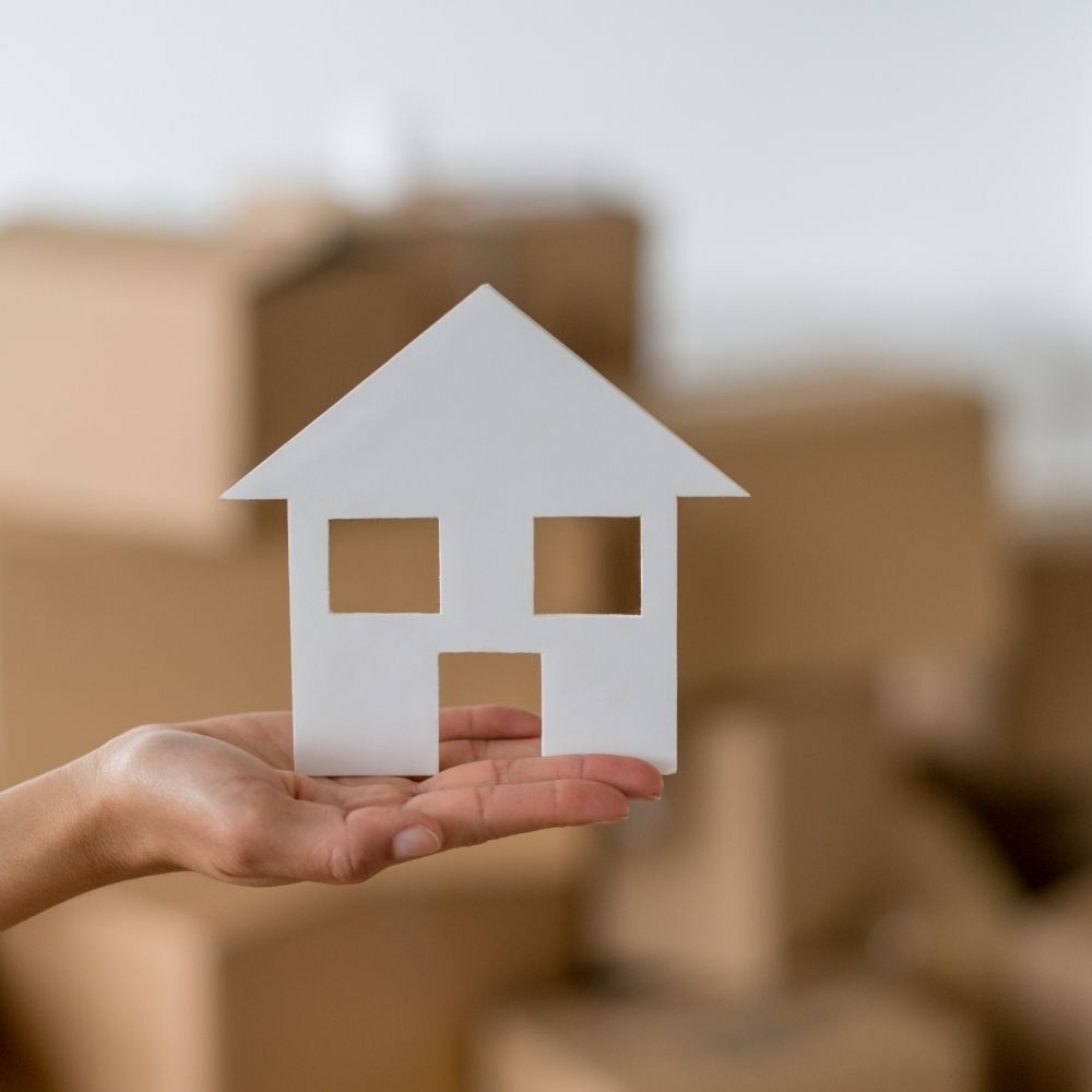 person holding a model house with boxes in the background