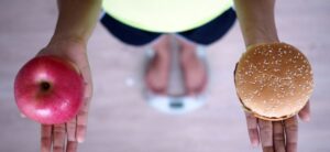 person stood on a scale holding a burger and an apple