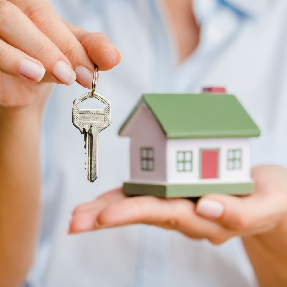 women holding a small model of a house and a key