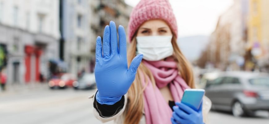 woman wearing a mask and gloves holding one hand out and her phone in the other