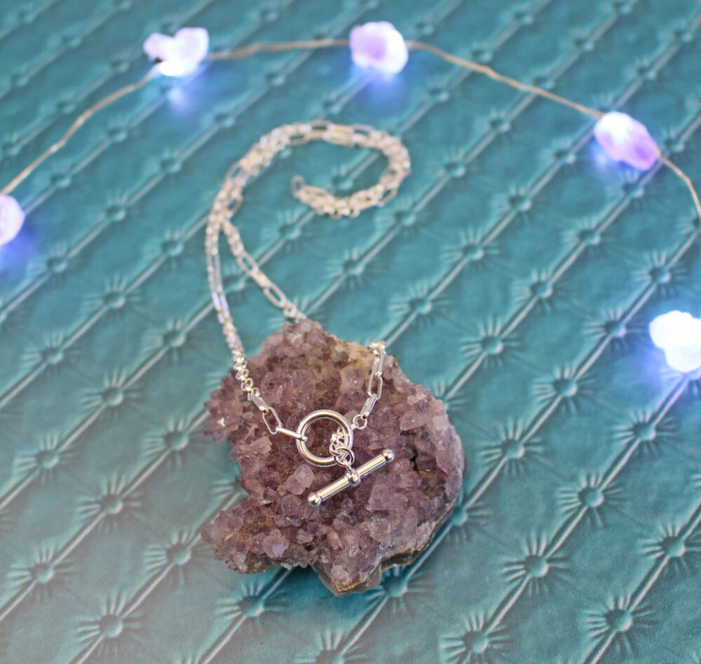 Estée Lalonde Interlock Chain Necklace Sterling Silver from Daisy London with lights in behind it and onto top a piece of amethyst