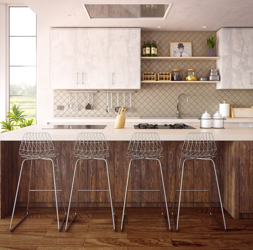 Modern kitchen with a wooden island and four wire bar stools. White cabinets, a tiled backsplash, and shelves with various kitchen items enhance the decor. Sunlight streams through a large window, illuminating the room.