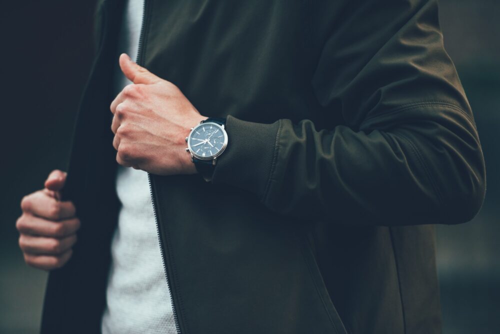 man wearing a light tshirt and dark jacket with a watch on
