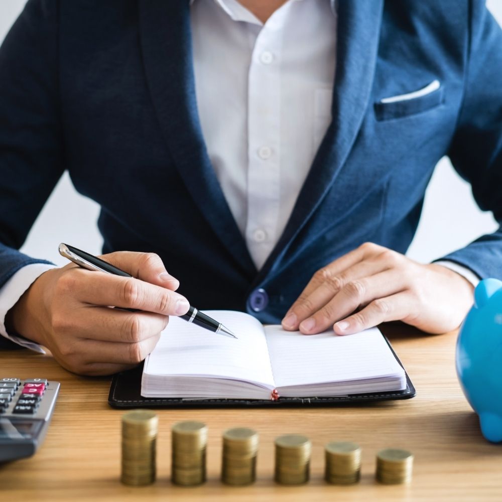 man sat with a pen writing in a note book with coins infront