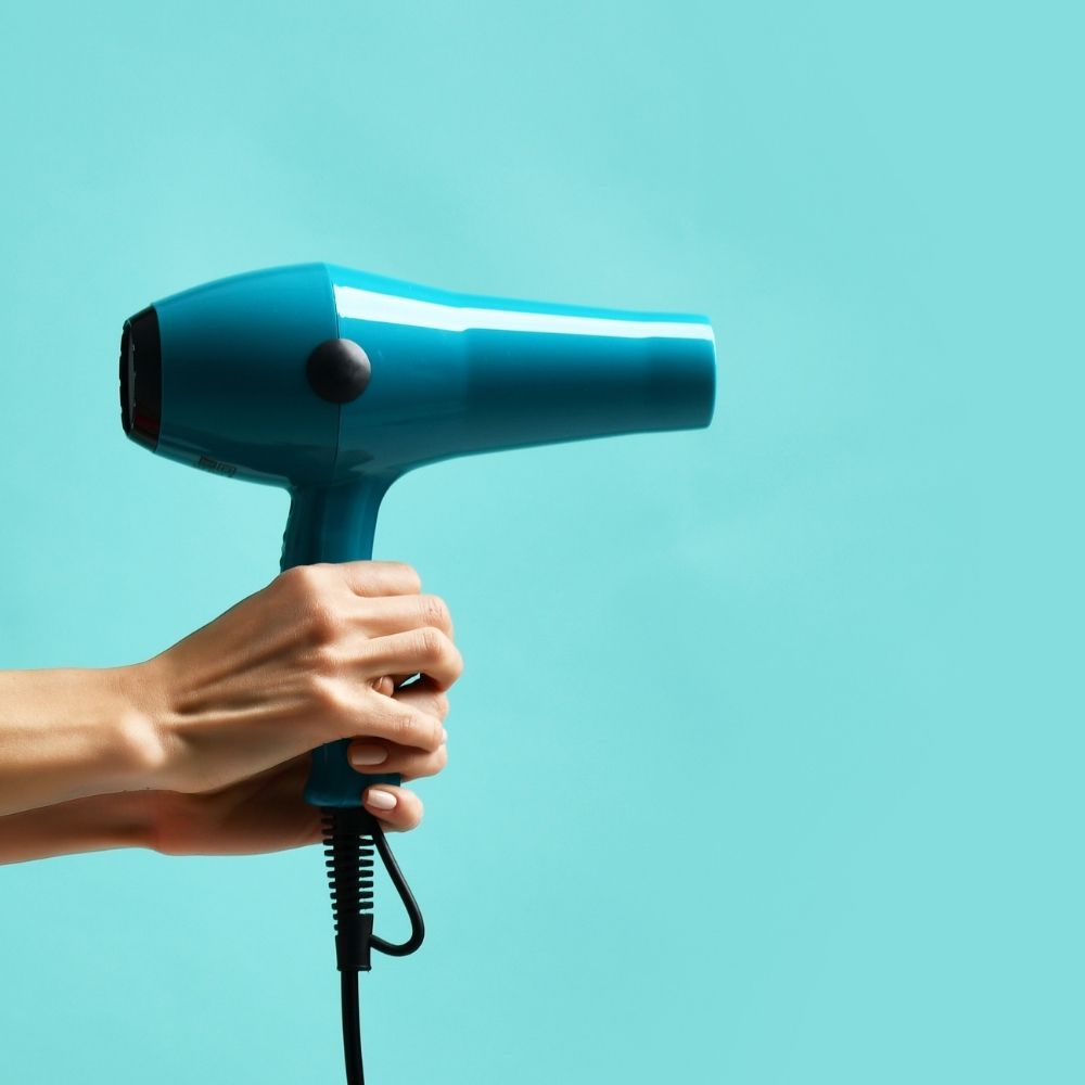 person holding a hairy dryer against a blue backdrop