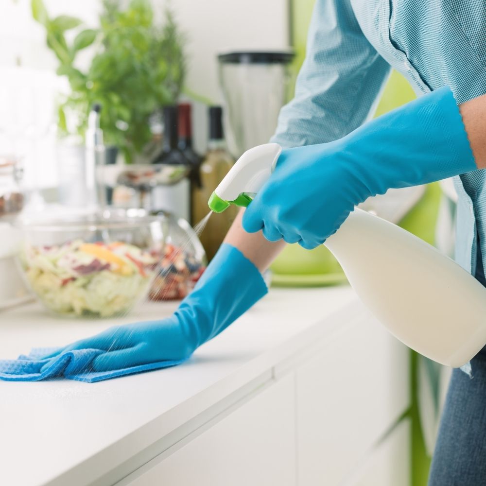 person wearing blue rubber gloves and holding a cleaning spray bottle cleaning a work surface