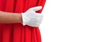 person wearing white glove opening a red curtain