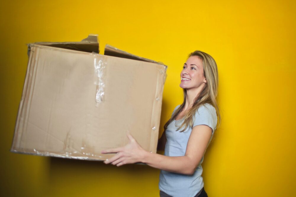 Woman holding a cardboard box against a yellow backdrop