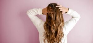 woman with her back to the camera with hands in her hair on a pick backdrop