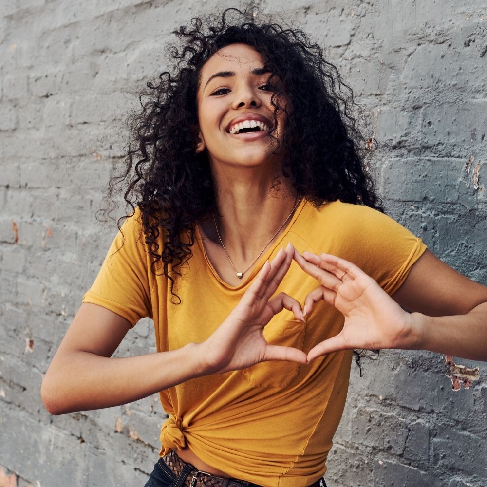 women weating a mustard top and making a heart shape with her hands