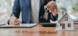 person holding a set of keys and signing a piece of paper by a house model