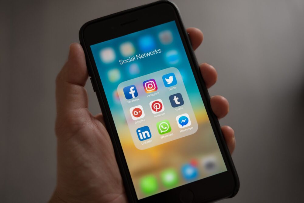 person holding a mobile phone with social media icons viewable