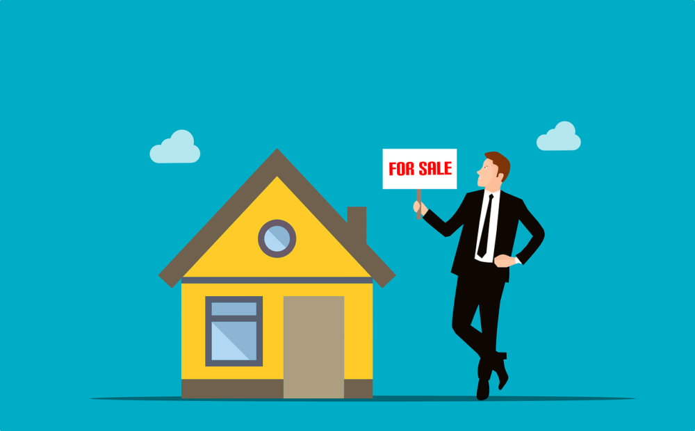 Person standing with a for sale sign beside a house