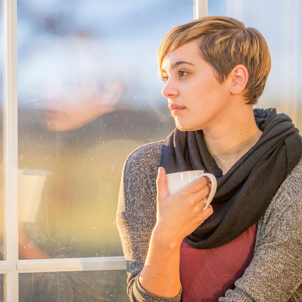 person sat holding a drink looking out a window