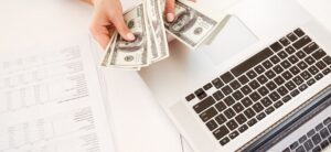 person sat in front of a computer with money in hand