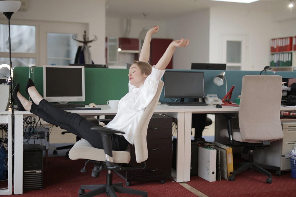 Person in the work place with her arms in the air and feet up