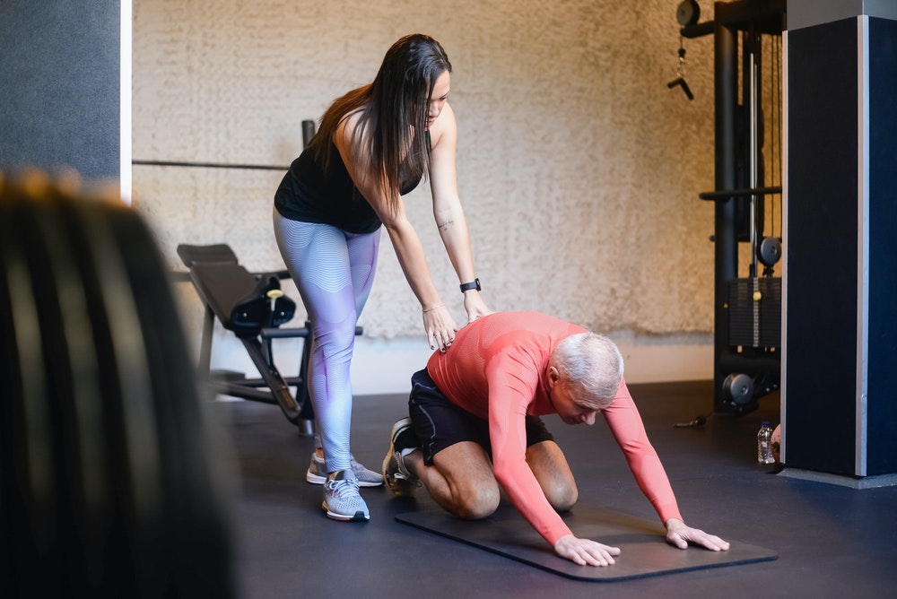 a personal trainer helping an older man stretch his body