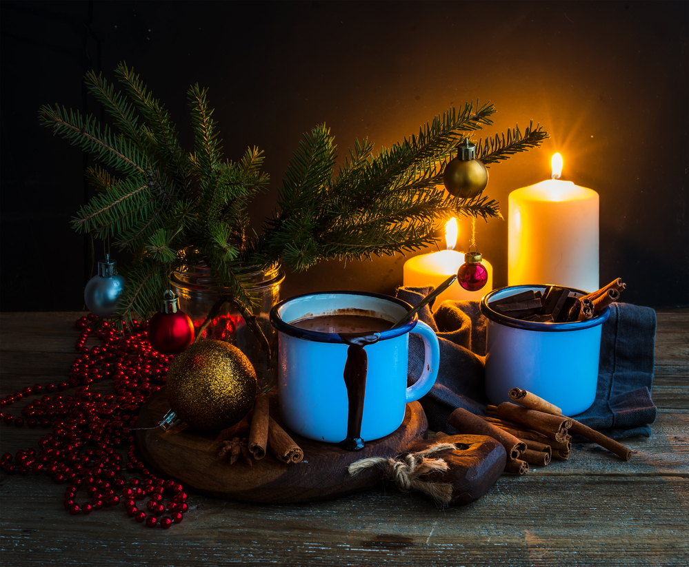 Christmas food and decorations set. Fur tree branches, mug of hot chocolate, colorful glass balls, burning candles and cinnamon sticks, dark background, selective focus