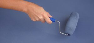 Womans hand painting a blue surface with a paintroller