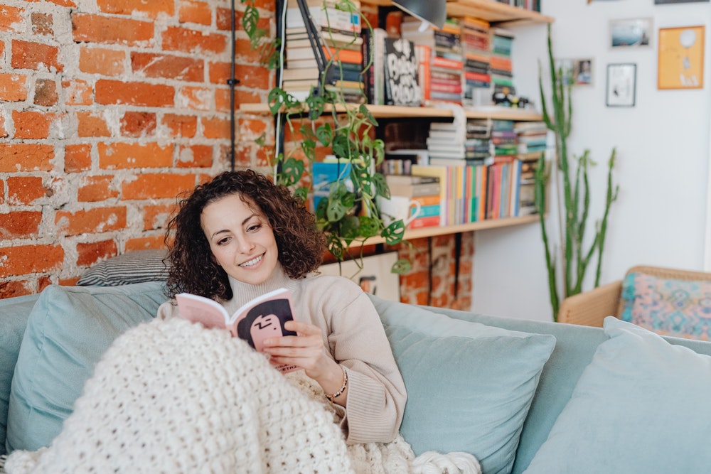 woman under a blanket reading a book