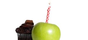 apple with a candle in it, in front of a chocolate muffin