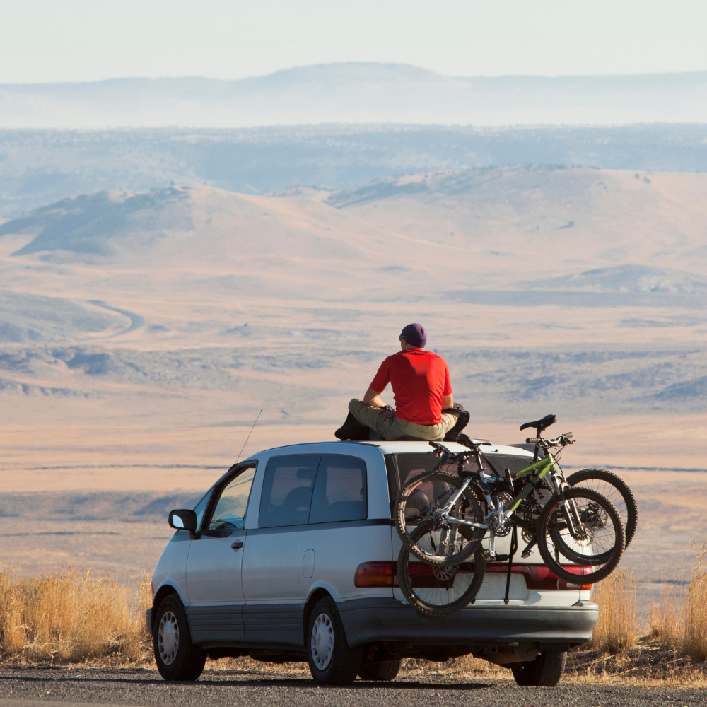 man sat on top of his car looking at the valley below