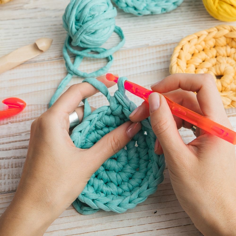 person crochet a round circle in turquoise with a yellow one sat on the table nearby