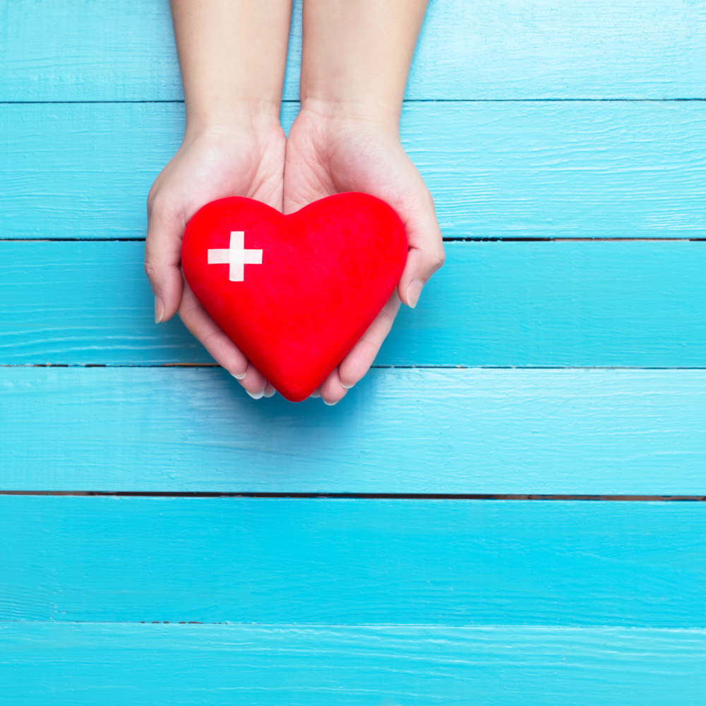 person holding a red heart in their hands against a blue backdrop