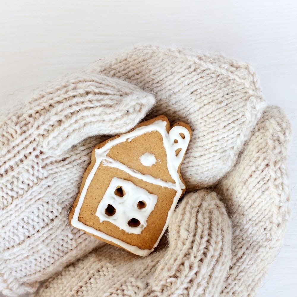 person wearing white mittens holding a cookie house