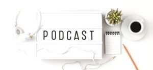 PODCAST written on a lightbox with headphones notebook and coffee beside