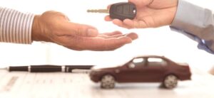person passing over a car key with a small car and pen in the background
