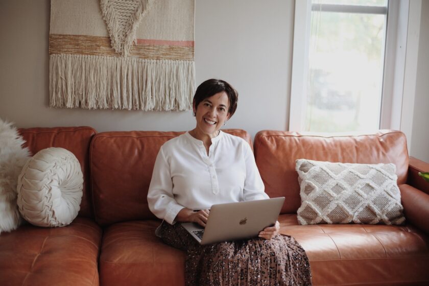 woman in a white shirt sat on a sofa looking at a laptop