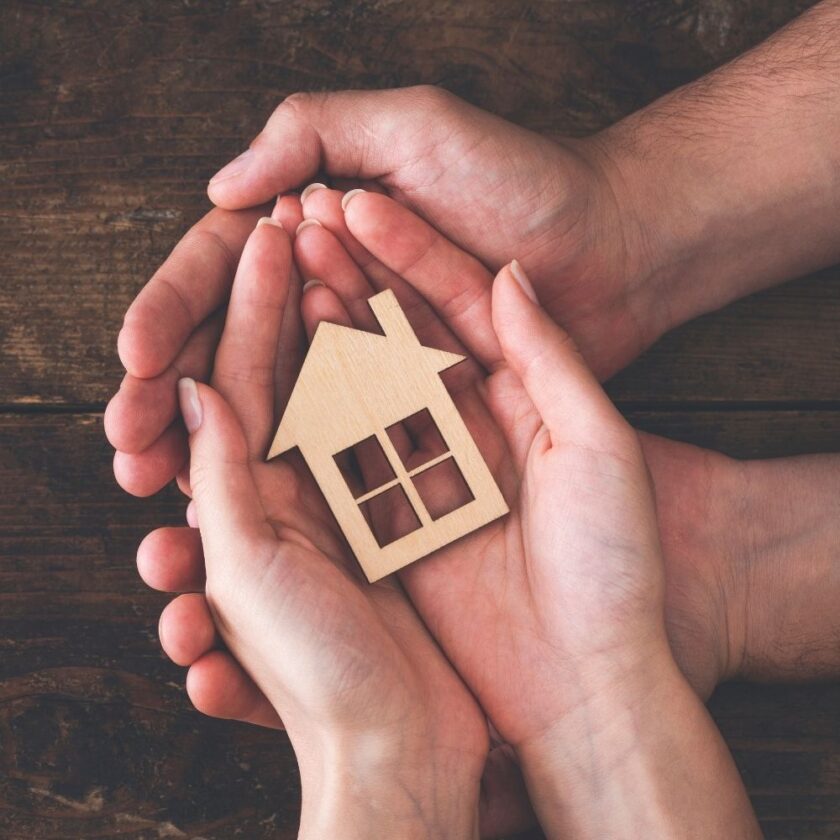 two people holding a wooden shape of a home