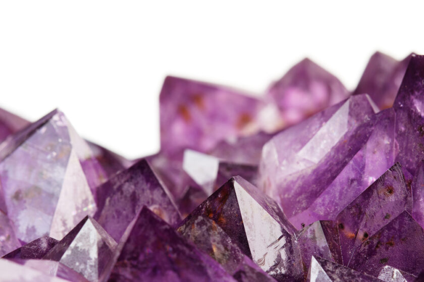 Close-up of several amethyst crystals with sharp, faceted points. Embraced for their crystal healing properties, these gems display a vibrant purple hue with varying opacities, set against a plain white background.