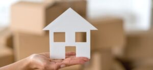 person holding a cut out house with boxes behind