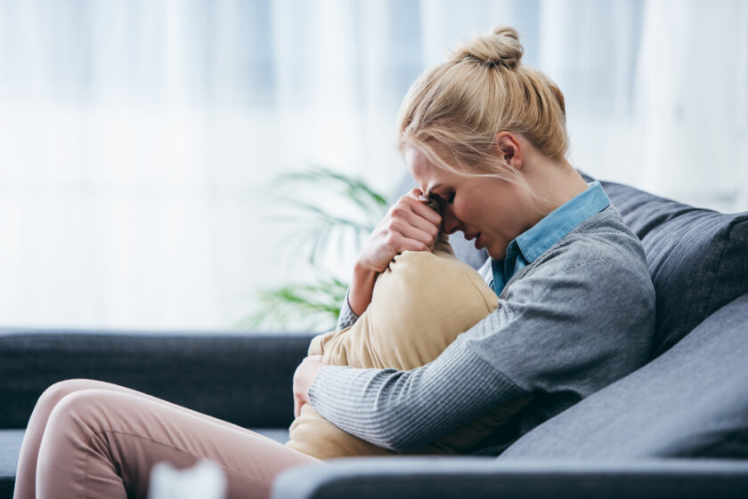 upset woman holding a cushion and sat on a sofa image licensed via deposit photos