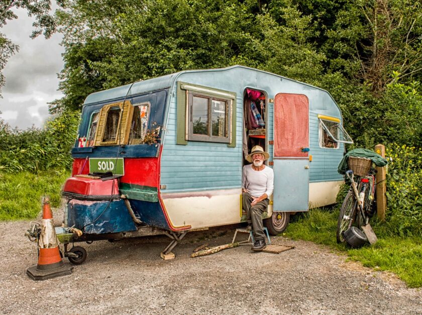 man in a white shirt sat in the door of a caravan