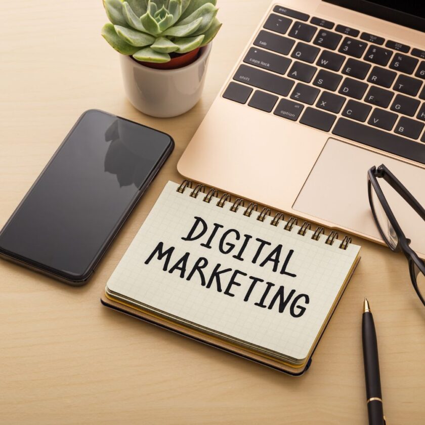 digital marketing written on a note pad by a computer and phone